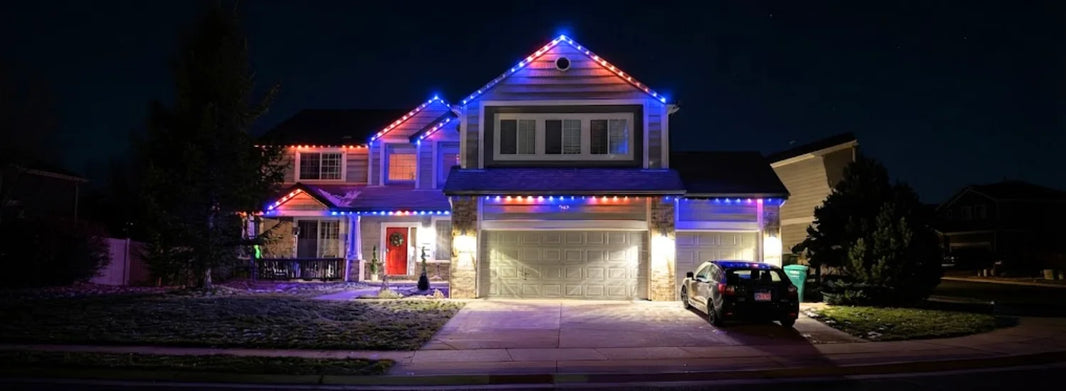 A suburban family home at night, lit up by blue and orange Christmas lights strung along the edges of the roof.