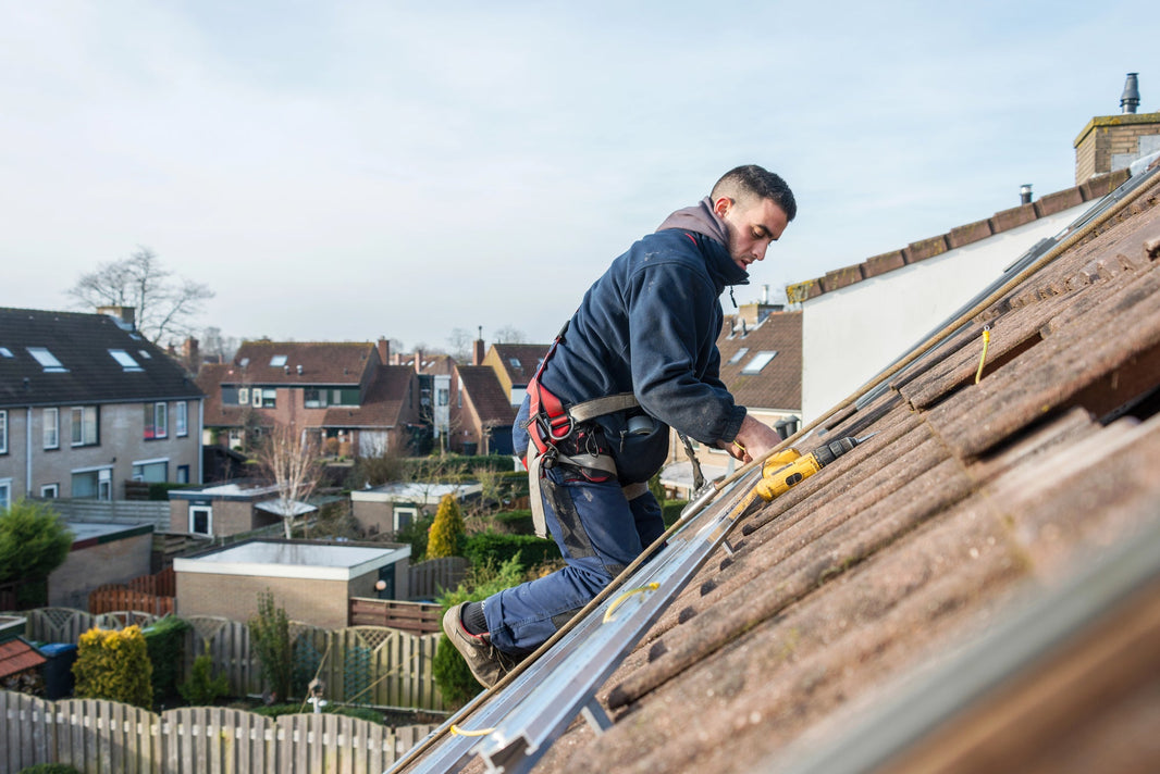 A general contractor on a roof, making various markings with their tools, with an upscale residential neighborhood in the background.