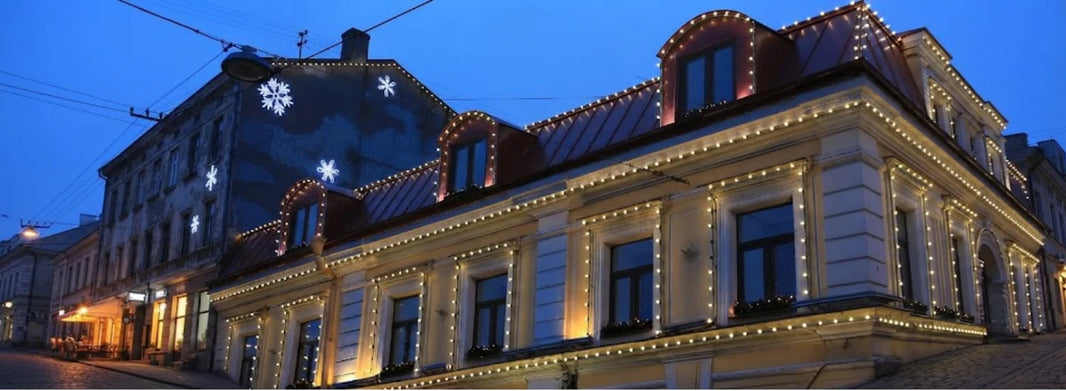 The outside of a building with many windows, all of which are ringed with warm yellow decorative lights against a blue evening sky.