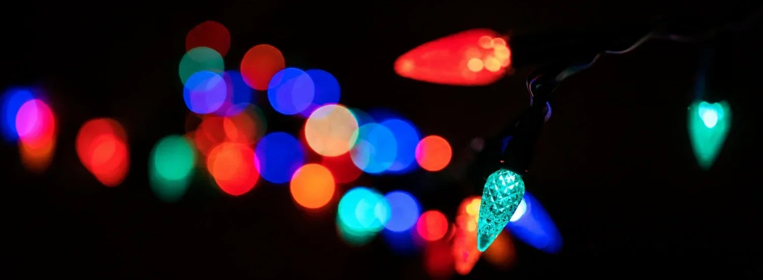 A bright, green C9 bulb Christmas light against a black background, in which several blurred lights of other colors are visible farther away.