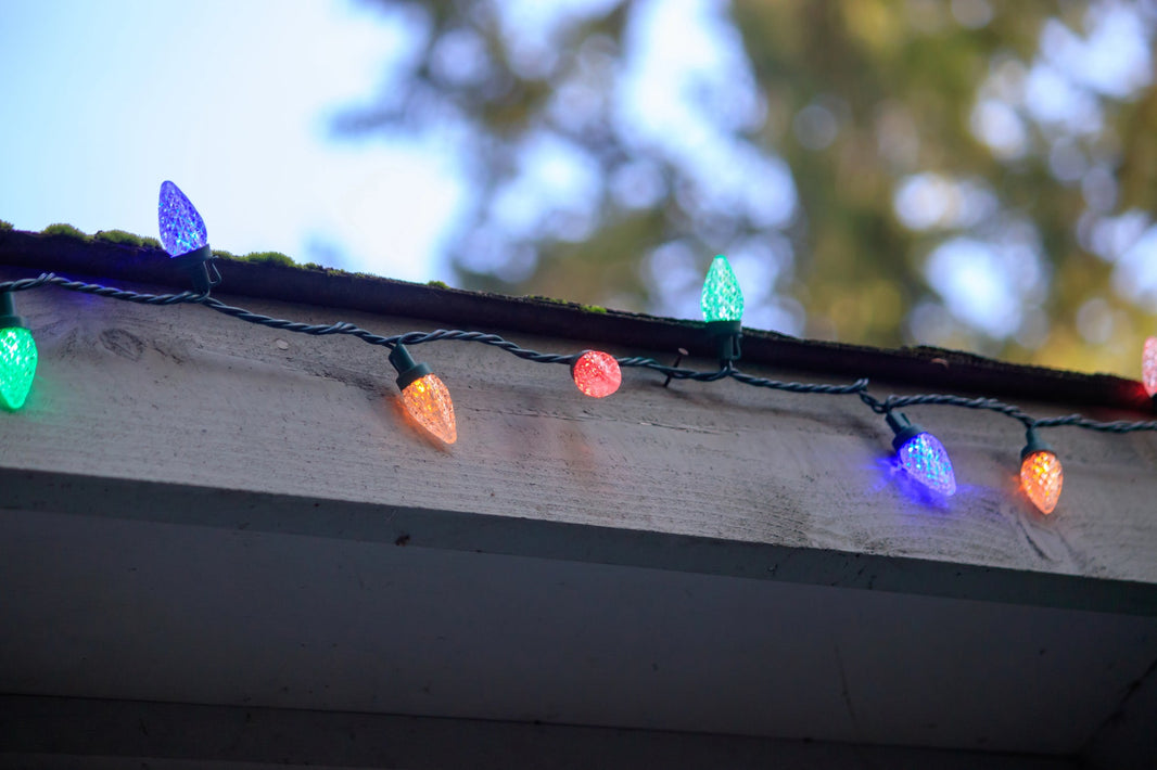 Faceted C9 bulbs of various colors against a wooden awning in daytime.